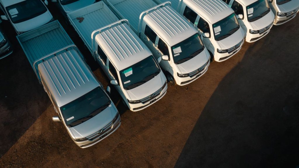 Aerial view of white pickup trucks aligned neatly in a parking lot. High contrast lighting.