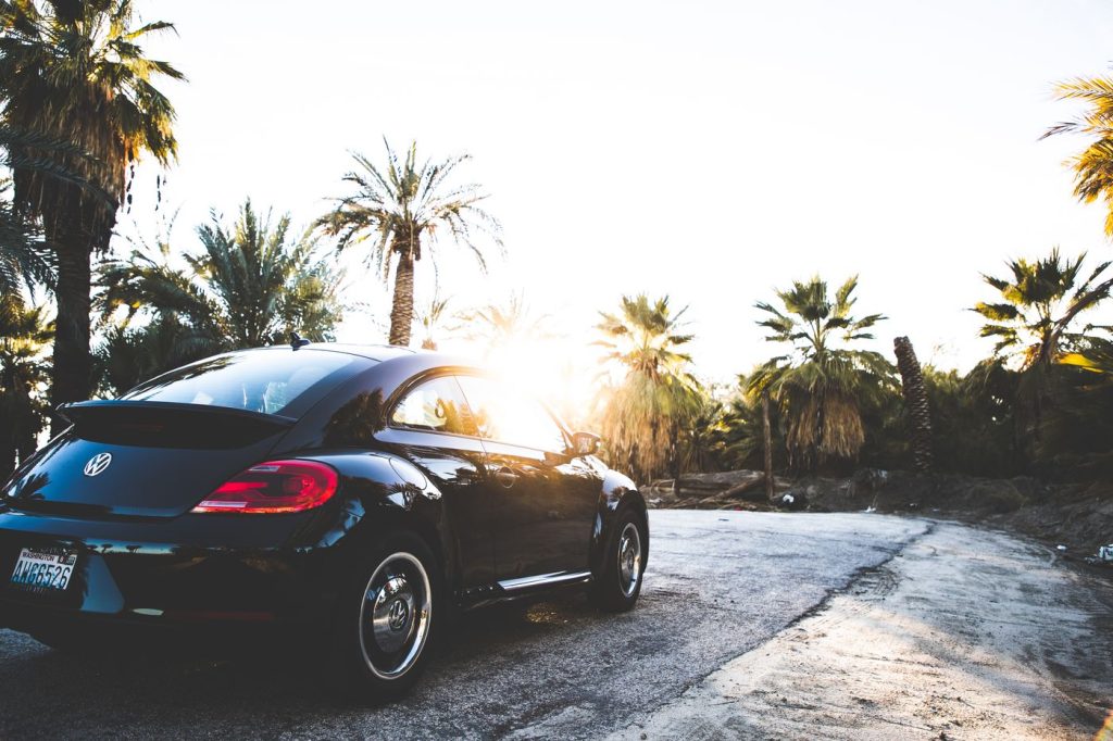 A luxurious black car parked on a tropical road surrounded by palm trees at sunset, perfect for travel and vacation themes.