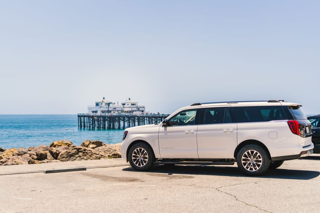 A luxury SUV parked near the iconic Malibu Pier with a stunning ocean view on a sunny day.