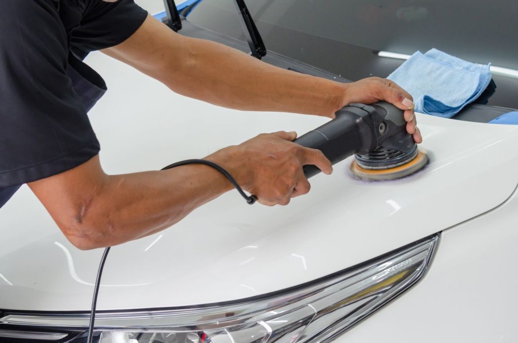 Close-up of a mechanic using a rotary polisher on a white car bonnet for detailing.
